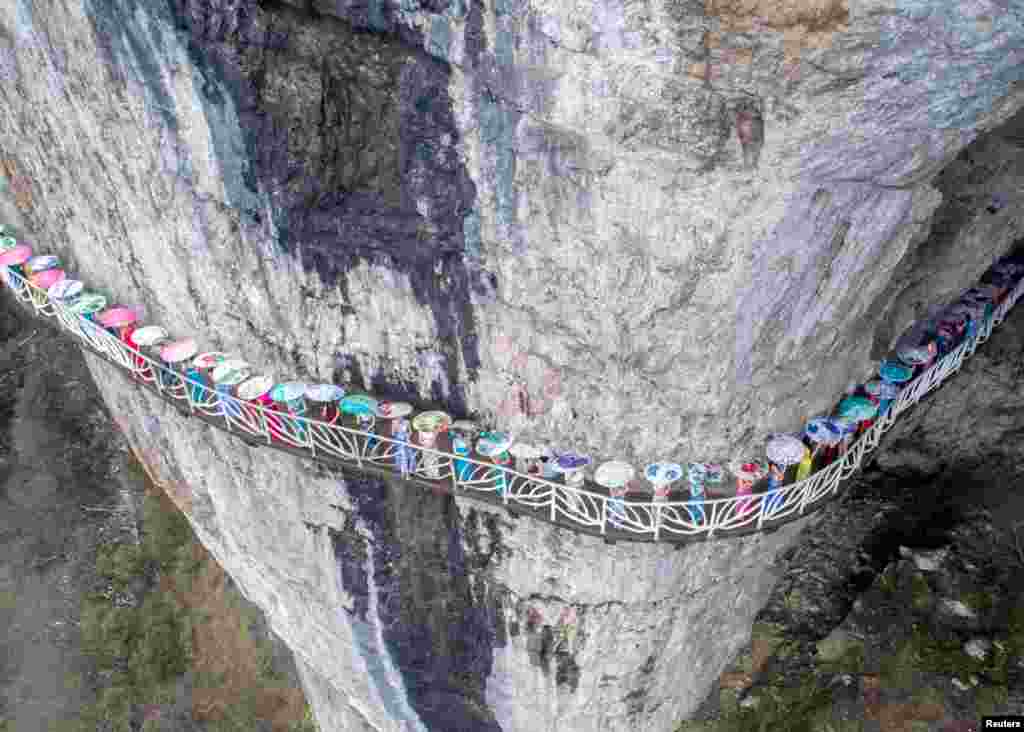 Para perempuan mengenakan pakain tradisional cheongsam dan berpayung, berpose di jalan setapak di sebuah tebing di kota Chongqing, China.