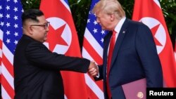 U.S. President Donald Trump and North Korea's leader Kim Jong Un shake hands during the signing of a document after their summit at the Capella Hotel on Sentosa island in Singapore, June 12, 2018. 