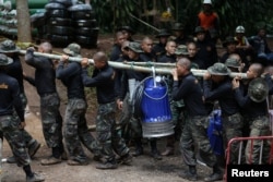 Military personnel carry a water pump machine as they enter the Tham Luang cave complex, where 12 boys and their soccer coach are trapped, in the northern province of Chiang Rai, Thailand, July 6, 2018.