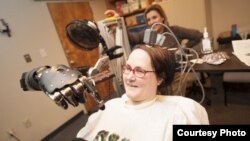 Jan Scheuermann, who has quadriplegia, brings a chocolate bar to her mouth using a robot arm she is guiding with her thoughts. Researcher Elke Brown, M.D., watches in the background. Click the photo to download it in high resolution, Photo credit: "UPMC"