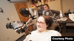 Jan Scheuermann, who has quadriplegia, brings a chocolate bar to her mouth using a robot arm she is guiding with her thoughts. Researcher Elke Brown, M.D., watches in the background, Photo credit: "UPMC"