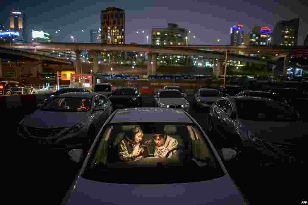 A couple look at a mobile phone as they sit in a car at a screening at a drive-through cinema in Seoul, South Korea, March 21, 2020.