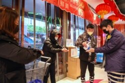 Seorang karyawan membagikan cairan desinfektan kepada pelanggan di pintu masuk sebuah supermarket di Wuhan, di Provinsi Hubei, di Cina tengah Sabtu, 25 Januari 2020. (Chinatopix via AP)