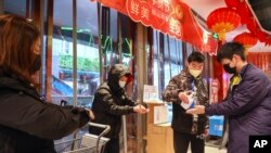 Un empleado distribuye desinfectante a clientes a la entrada de un supermercado en Wuhan, en la provincia de Hubei, en el centro de China, el sábado 25 de enero de 2020, debido a una epidemia de un mortal virus que afecta las vías respiratorias. (Chinatopix vía AP)