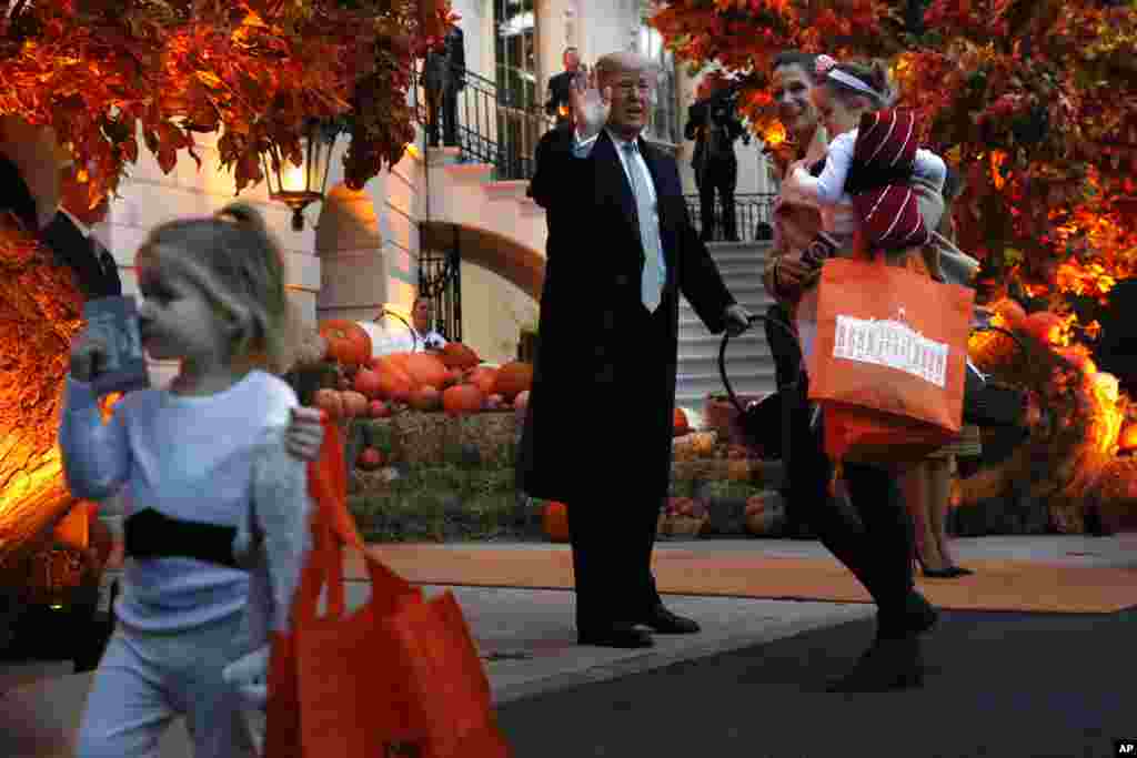 白宫万圣节活动中，家长抱着孩子领取总统唐纳德&middot;特朗普和第一夫人梅拉尼娅&middot;特朗普发的糖果（2018年10月28日）。