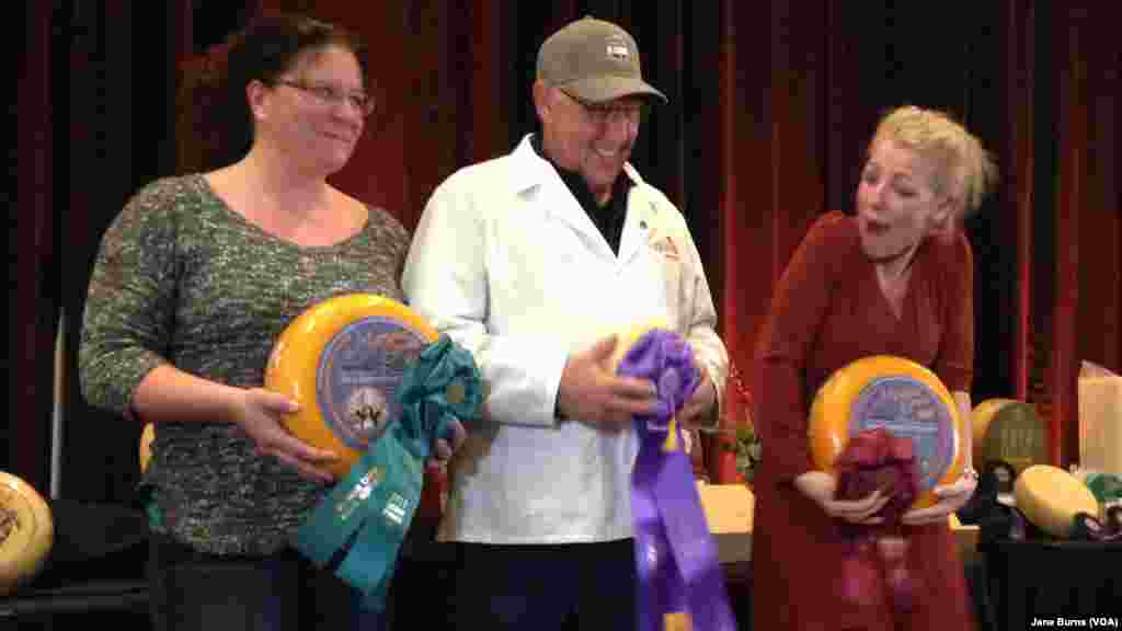 Richard Guggiesberg (center) cradles his champion Baby Swiss cheese. Marieke Penterman (right), whose cheeses placed second and third in the competition, and general manager of her company, Kim Raybuck, also pose on the winners podium, in Green Bay, Wis.,