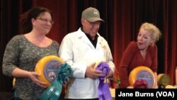 Richard Guggiesberg, center, cradles his champion Baby Swiss cheese. Marieke Penterman, right, whose cheeses placed second and third in the competition, and general manager of her company, Kim Raybuck, also pose on the winners podium, in Green Bay, Wis.