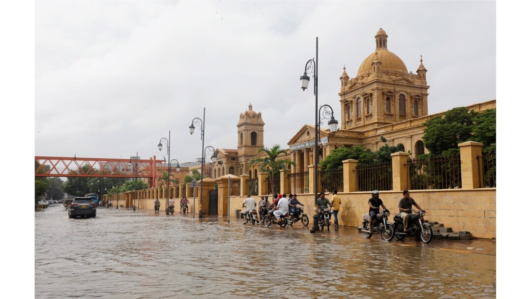 Pengendara sepeda motor lewat trotoar untuk menghindari jalanan yang tergenang banjir di depan Kampus Dayaram Jethamal Science yang dibangun pada masa kolonial Inggris, 27 Agustus 2020.