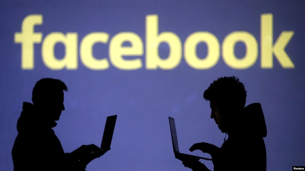 Silhouettes of laptop users are seen next to a screen projection of Facebook logo in this picture illustration taken March 28, 2018.