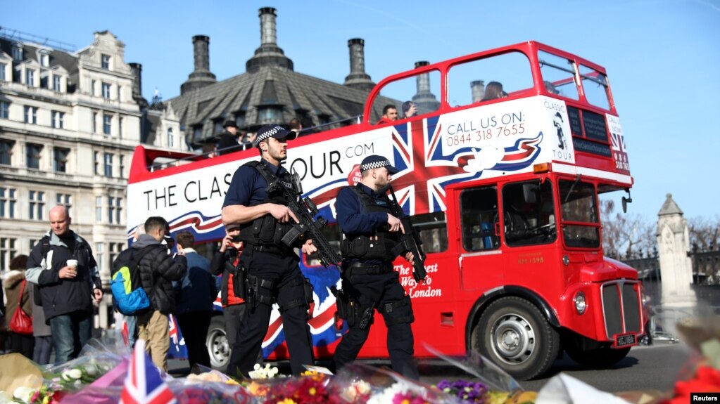 Des policiers armés devant des fleurs déposées en hommage des victimes des attentats de Londres. Grande Bretagne, 24 mars 2017.