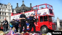 Des policiers armés devant des fleurs déposées en hommage des victimes des attentats de Londres. Grande Bretagne, 24 mars 2017. 