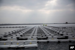FILE - Contractors work on a floating solar panel array on the Queen Elizabeth II Reservoir near Walton-on-Thames in southwest London, March 21, 2016. Britain's unique climate is seen as having contributed to its reaching its current capacity of renewables.