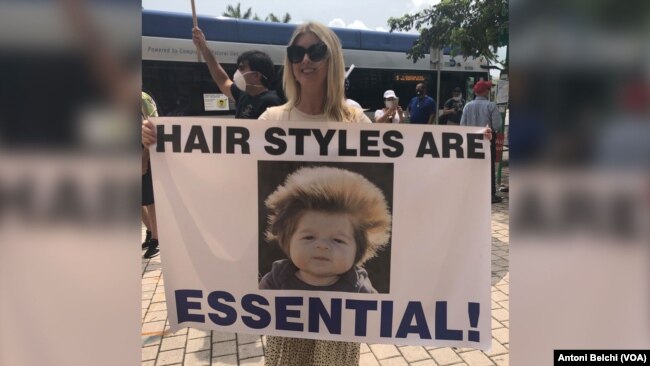 Una mujer sostiene un cartel con el lema "Los peinados también son esenciales" durante una protesta en Miami para pedir la reapertura de Florida durante la pandemia del coronavirus.