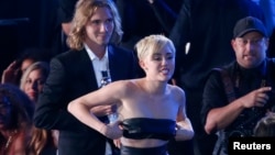 Miley Cyrus camina frente a su amigo Jesse Helt, (Izq.), a quien presentó al recibir el premio a Mejor Vídeo del año, por la canción "Wrecking Ball", en la gala de los premios MTV. 
