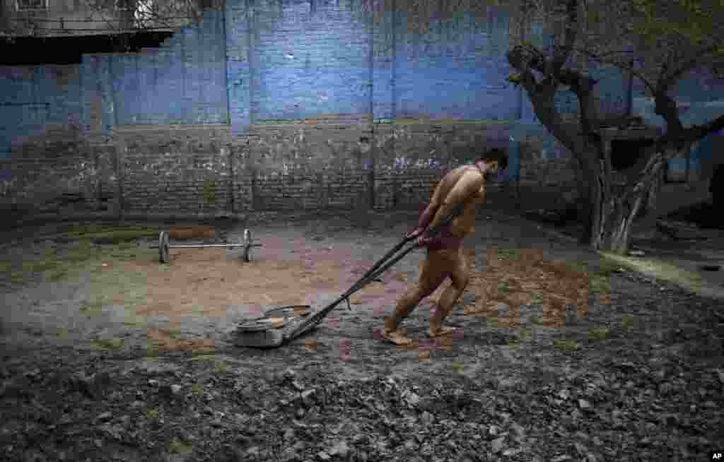 Seorang pegulat Kushti Pakistan mempersiapkan tanah di atas ring, sebelum sesi latihan harian mereka, di sebuah klub gulat di Lahore.