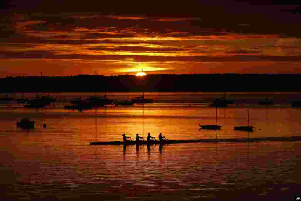 A quad scull of rowers begin their workout on Casco Bay as the sun starts to peak over Great Diamond Island in Portland, Maine.