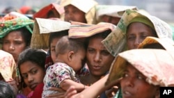 FILE - A Bangladeshi woman shields her baby from the sun as she stands in a line at a rice shop in Dhaka, April 5, 2008.