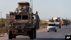 FILE - A convoy of U.S. troops drive along a road with local allied fighters, in Manbij, northern Syria, March 31, 2018.