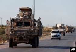FILE - A convoy of U.S. troops moves along a road with local allied fighters, in Manbij, northern Syria, March 31, 2018.