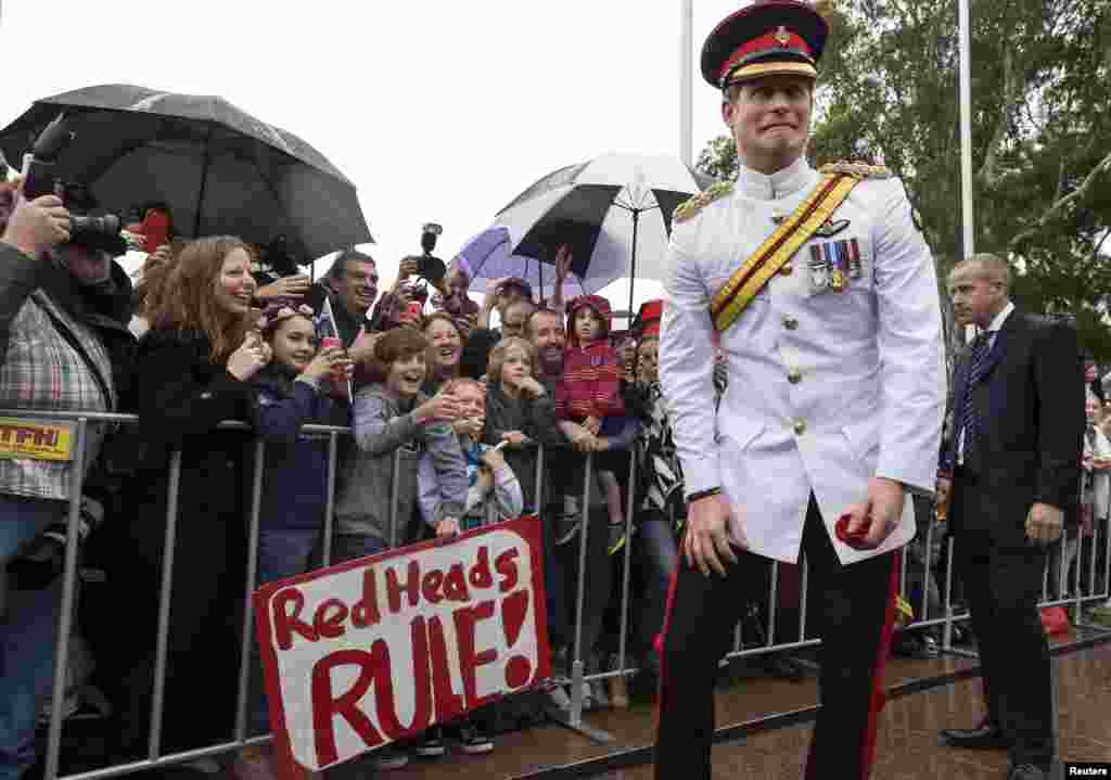 Britain&#39;s Prince Harry reacts as he shakes hands with members of the public displaying a sign reading &#39;Red Heads Rule&#39; after visiting the Australian War Memorial in Canberra.