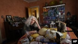 Phyllis Marder poses with her cat, Nellie, with food she recently obtained from a local food bank in the dining room of her home in Evanston, Ill. (AP Photo/Charles Rex Arbogast)