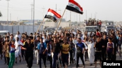 Volunteers, who have joined the Iraqi army to fight against militants from the radical Islamic State of Iraq and the Levant (ISIL), carry weapons and wave Iraqi flags during a parade in the streets of eastern Baghdad June 15, 2014.