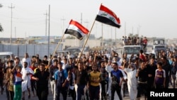 Các tình nguyện viên tham gia quân đội Iraq chiến đấu chống lại các phần tử chủ chiến của tổ chức Nhà nước Iraq và Levant (ISIL) đem theo vũ khí và vẫy cờ Iraq trong một cuộc tuần hành trên phố ở quận Al-Fdhiliya, miền đông Baghdad, 15/6/2014.