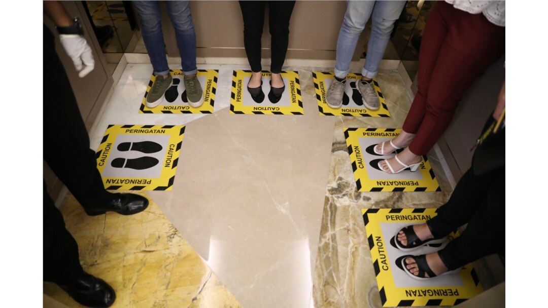 Para pengunjung berdiri di tempat yang sudah ditandai dalam sebuah lift untuk menjaga jarak aman sebagai upaya mencegah penularan virus corona, Surabaya, 19 Maret 2020. (Foto: AP)