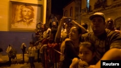 People watch a march in celebration of the 162nd birth anniversary of Cuba's independence hero Jose Marti beside an image of Cuban revolutionary hero Ernesto 'Che' Guevara on a wall in downtown Havana, Jan. 27, 2015. Thousands of members from the Cuban Communist Youth Union (UJC) and student organizations participated in the march.