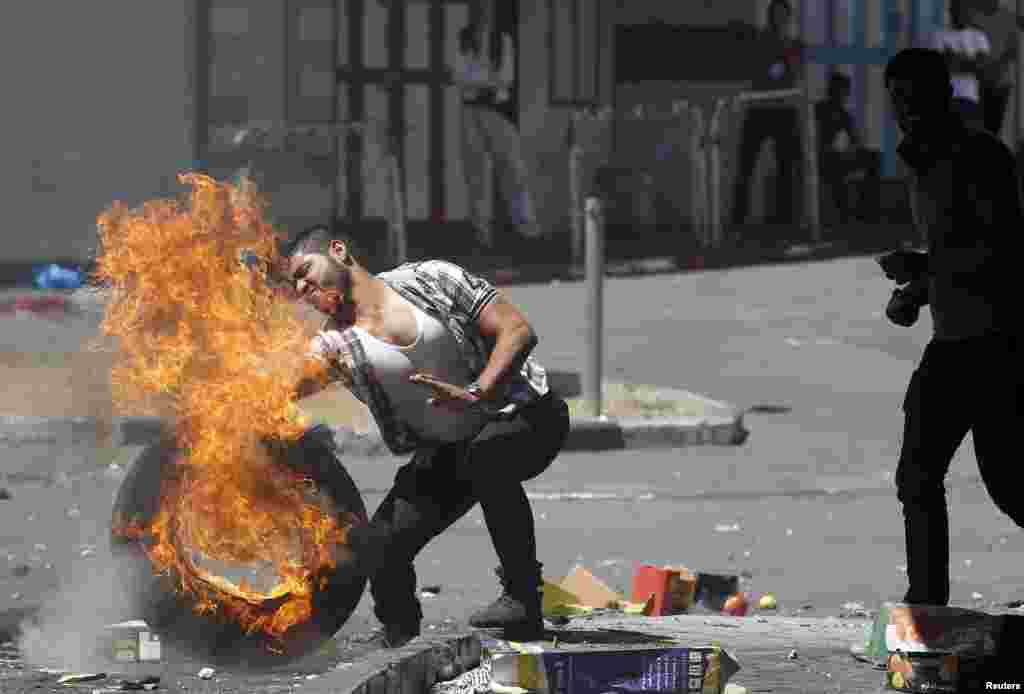 A man pushes a burning tire during a protest in Hebron, Aug. 22, 2014.
