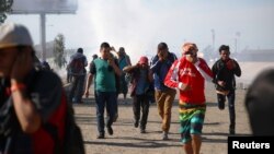 Мігранти прикривають свої обличчя, втікаючи від сльозогінного газу, застосованого прикордонним патрулем США біля огорожі між Мексикою та Сполученими Штатами в Тіхуані, Мексика, 25 листопада 2018 року.
