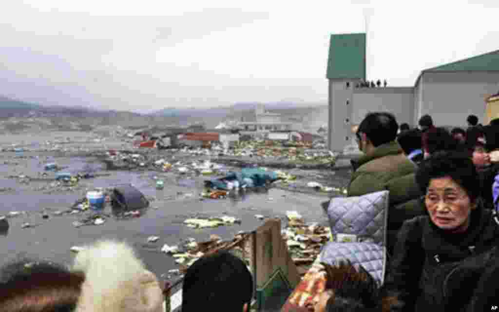 People watch the aftermath of tsunami tidal waves covering a port at Kesennuma in Miyagi Prefecture, northern Japan, after strong earthquakes hit the area, March 11, 2011 - (AP)