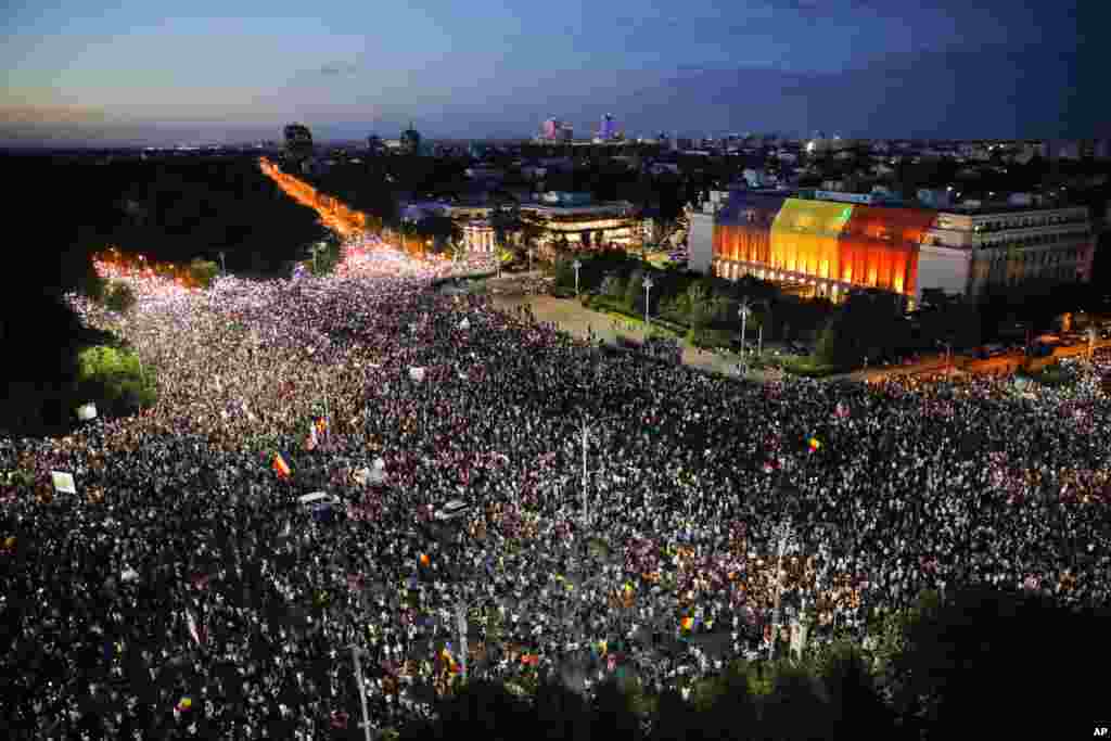 People shine the lights of their mobile phones during protests outside the government headquarters, seen at right, in Bucharest, Romania. Romanians who live abroad are staging an anti-government protest calling on the left-wing government to resign and an early election.