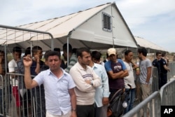 FILE - In this file photo taken on Monday, June 13, 2016, migrants who live in the Hellenikon refugee and migrant camp in Athens wait to register for asylum. A government official in Athens on Wednesday, Aug. 3, 2106.