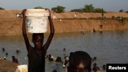 FILE - A girl carries a bucket filled with water from a pond in a camp for internally displaced persons at the United Nations base in Bentiu, Unity State, South Sudan.