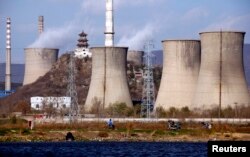 Fishermen sit beside a lake in front of the chimneys of a coal-burning power station located on the outskirts of Beijing November 22, 2011. REUTERS/David Gray