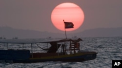 A Cambodian flag on a fishing boat flutters in wind as the sun sets over the Gulf of Thailand near Cambodia's port town of Sihanoukville.