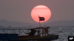 A Cambodian flag on a fishing boat flutters in wind as the sun sets over the Gulf of Thailand near Cambodia's port town of Sihanoukville.