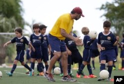 In this 2014 photo, Lee Santamaria, front, teaches children during a soccer camp held in Miami, Florida.