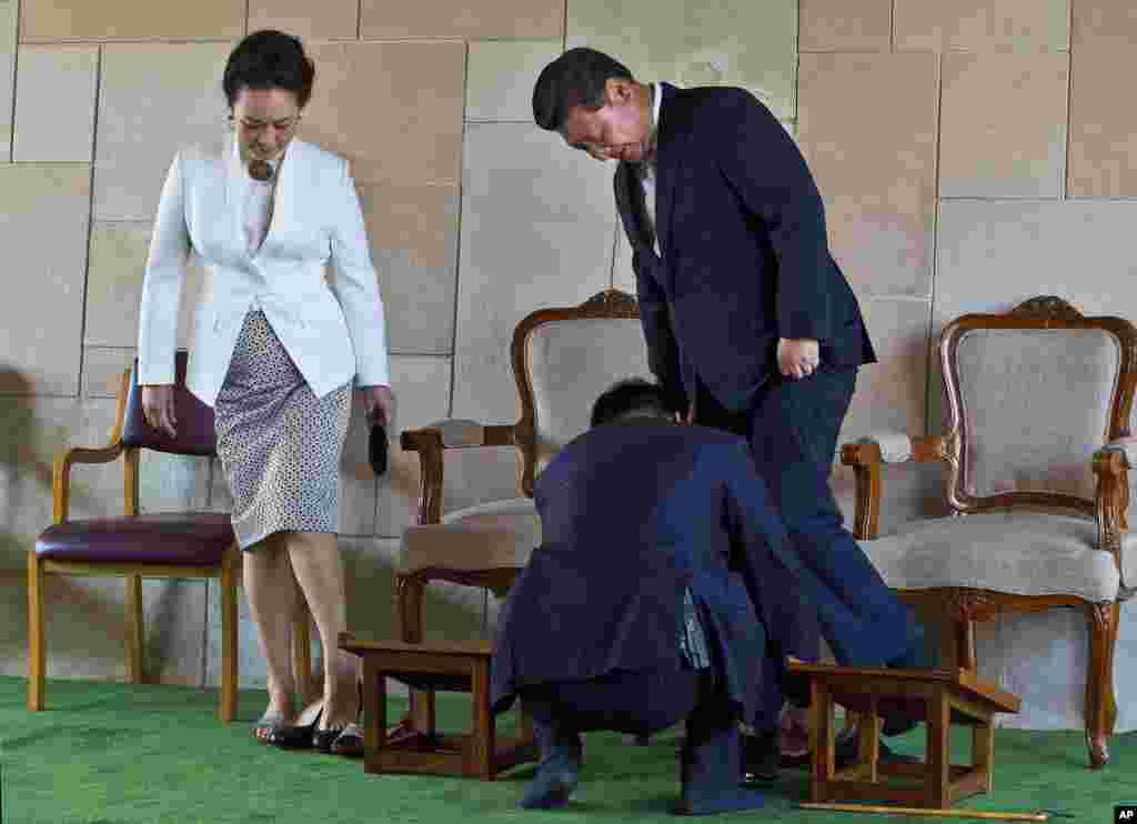 An aide helps Chinese President Xi Jinping tie his shoe, with his wife Peng Liyuan standing beside, after visiting Rajghat, the memorial to India's independence leader Mohandas Gandhi, more popularly called Mahatma Gandhi, in New Delhi, India.