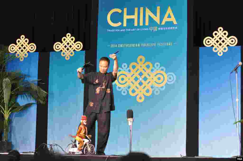 A Chinese puppeteer entertains the crowd with the antics of his monkey on a bicycle at the Smithsonian Folklife Festival in Washington, June 25, 2014. (Regina Catipon/VOA) 