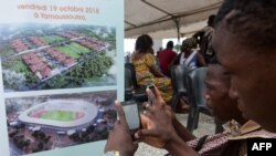 Les gens prennent des photos d'une pancarte représentant un futur stade à Yamoussoukro, le 19 octobre 2018.