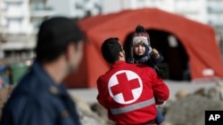 A Red Cross volunteer carries a child just disembarked from a crippled freighter carrying hundreds of refugees trying to migrate to Europe, at the coastal Cretan port of Ierapetra, Greece, on Thursday, Nov. 27, 2014. 