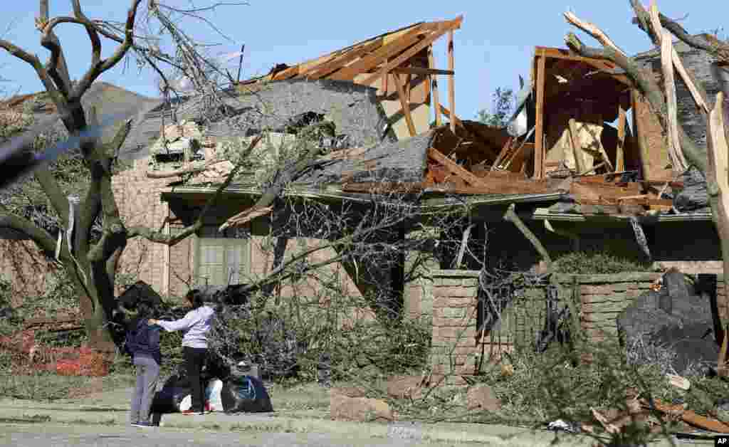 Women stand outside a house damaged by a tornado in the Preston Hollow section of Dallas.