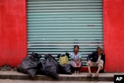 A couple sits with their belongings on the sidewalk, in front of a closed shop in Tepeojuma, Mexico, Sept. 24, 2017.
