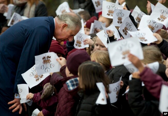 Schoolchildren wave images of the heraldic cypher of Britain's Prince Charles, as he bends down to talk to some of them, after he made a visit to meet Iraqi Christians in London, Dec. 9, 2014.