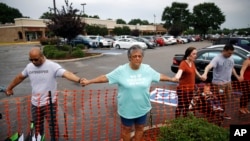 Lisa Dunaway (centro), residente de Virginia Beach, Virginia, se da la mano con recolectores de basura de la ciudad durante una vigilia en respuesta a un tiroteo en un edificio municipal. 1 de junio de 2019.