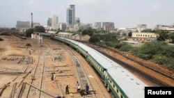 A passenger train moves past labourers working on a railway track along City Station in Karachi