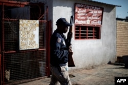 FILE - A South African police officer holds a rifle as he stands in Soweto, Johannesburg, Aug. 29, 2018, during unrest that erupted after a foreign shop owner allegedly shot and killed a member of the community during a demonstration.