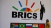 រូបឯកសារ៖ មន្ត្រីគណៈប្រតិភូម្នាក់ដើរកាត់ផ្លាក BRICS មុនកិច្ចប្រជុំកំពូល BRICS លើកទី ១០ នៅក្រុង Sandton នៃប្រទេសអាហ្វ្រិកខាងត្បូង កាលពីថ្ងៃទី ២៤ ខែកក្កដា ឆ្នាំ ២០១៨។ 